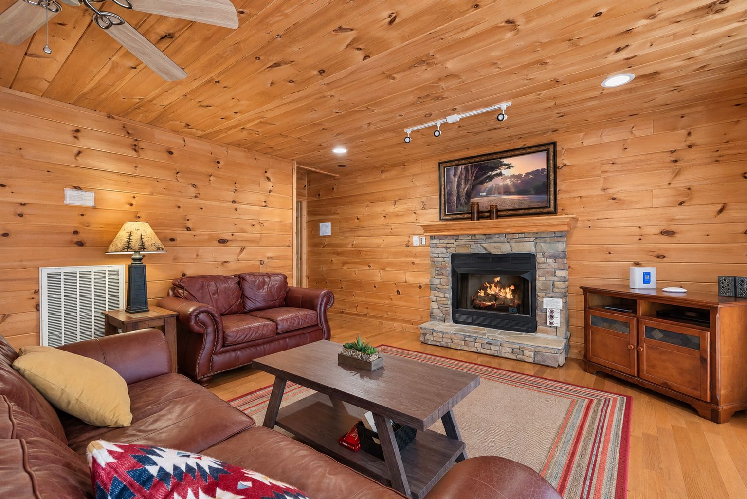 A cozy cabin interior with a leather sofa, a coffee table, a fireplace, and wooden walls.