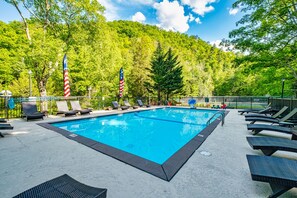 Ein Schwimmbecken mit Liegestühlen und amerikanischen Flaggen, umgeben von Bäumen und einer hügeligen Landschaft.