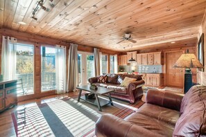 Een gezellig ingerichte kamer in chaletstijl, met houten plafond, leren bank, salontafel en een keuken voorzien van houten kastjes.