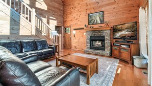 A cozy living room with a fireplace, leather sofa, and a stone fireplace surround. - Free Dollywood Tickets, Sauna, Hot Tub, Secluded Modern Cabin, Dogs OK (Sevierville)