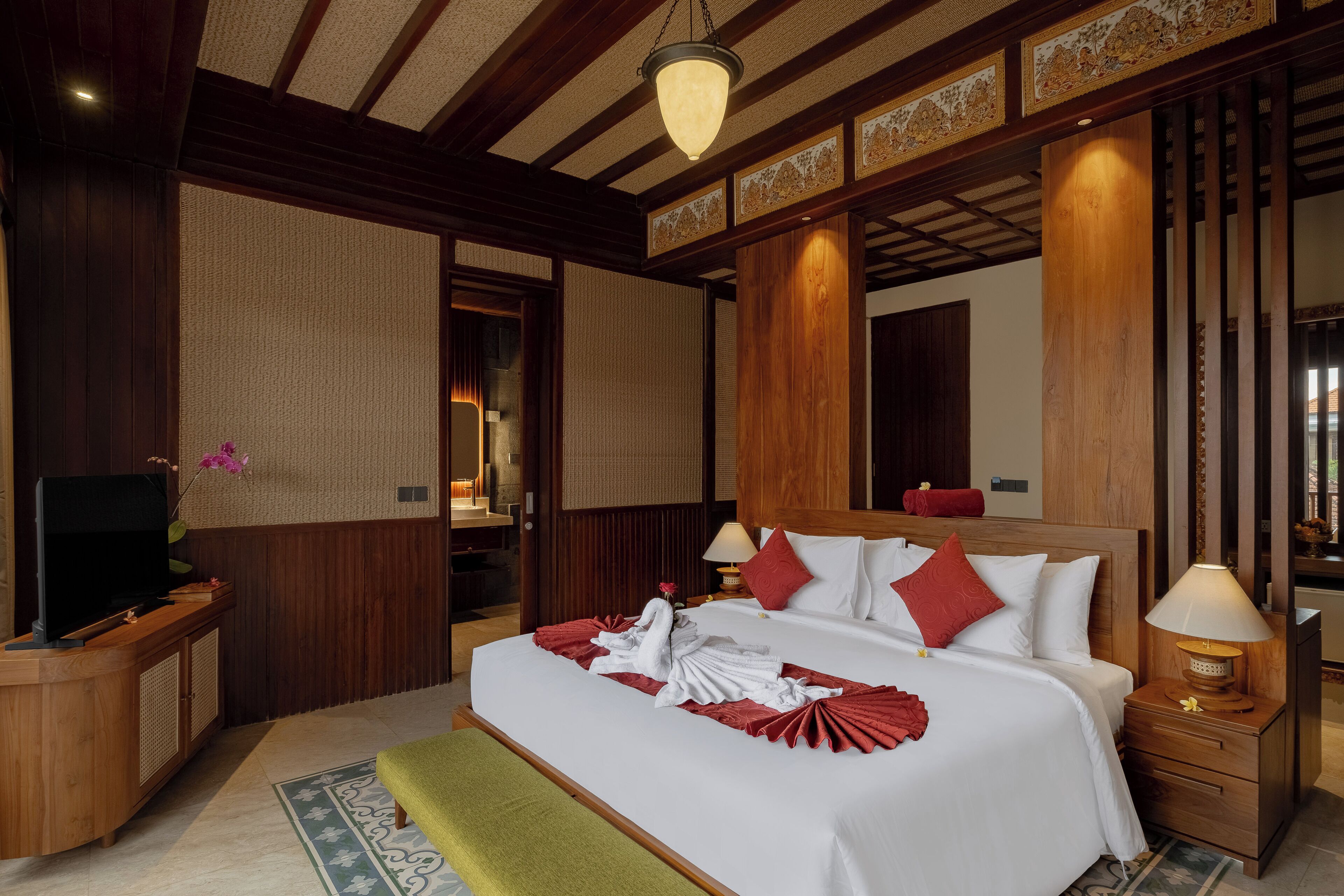A hotel room with a large bed, wooden headboard, bedside tables with lamps, a television on a wooden cabinet, and a decorative mirror.