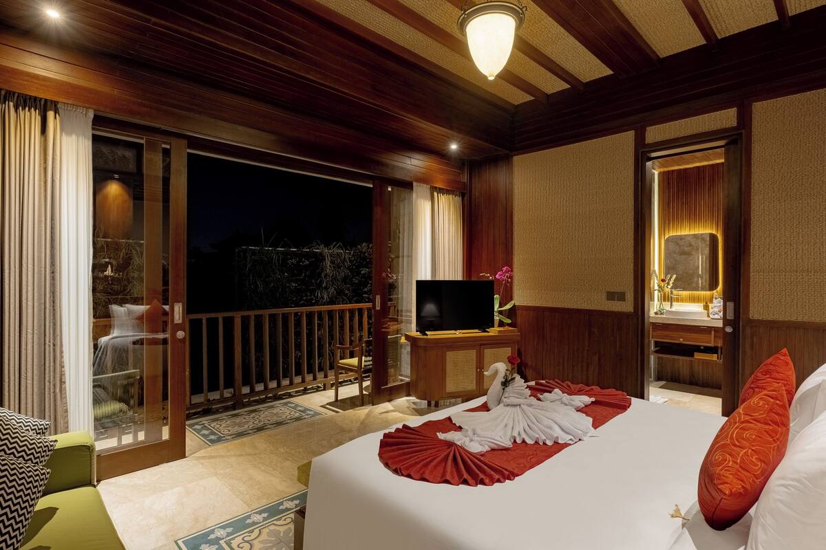 A hotel room with a bed, a television, a wooden cabinet, and a balcony with a view of the night sky.