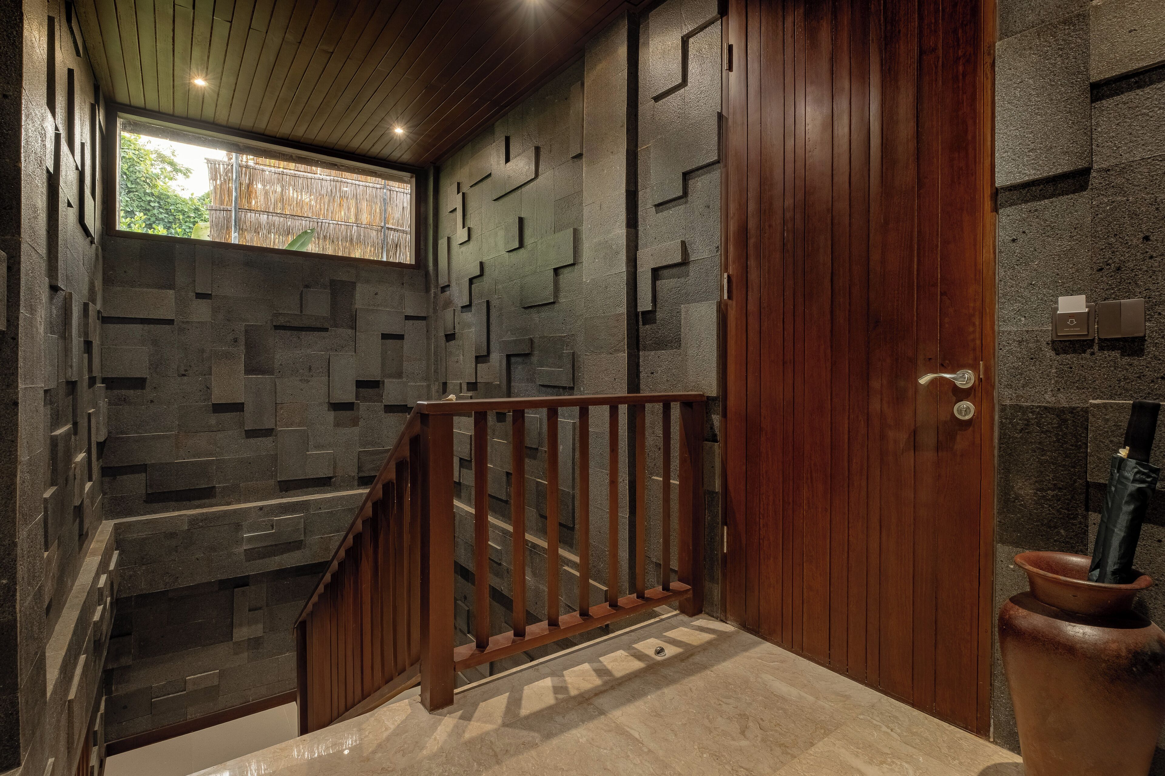 A staircase with a wooden railing, a wooden door, and a stone wall with geometric patterns.