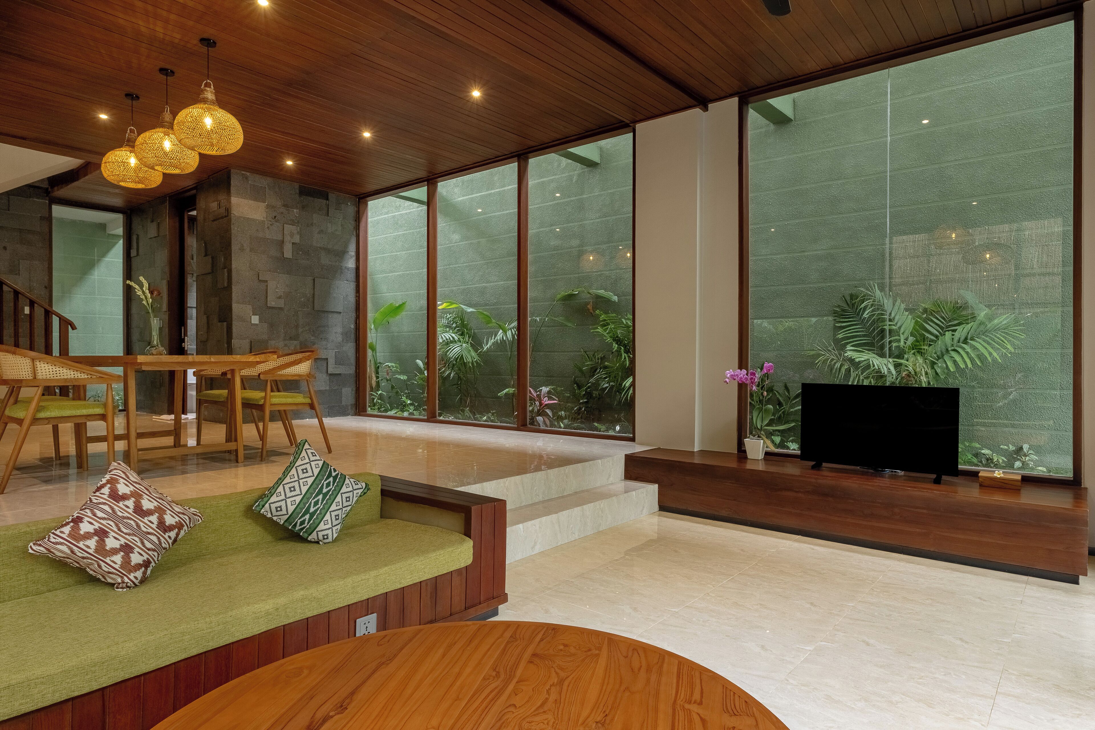 Una sala de estar moderna con techo de madera, ventanas amplias, televisor de pantalla plana y zona de comedor con mobiliario de madera.