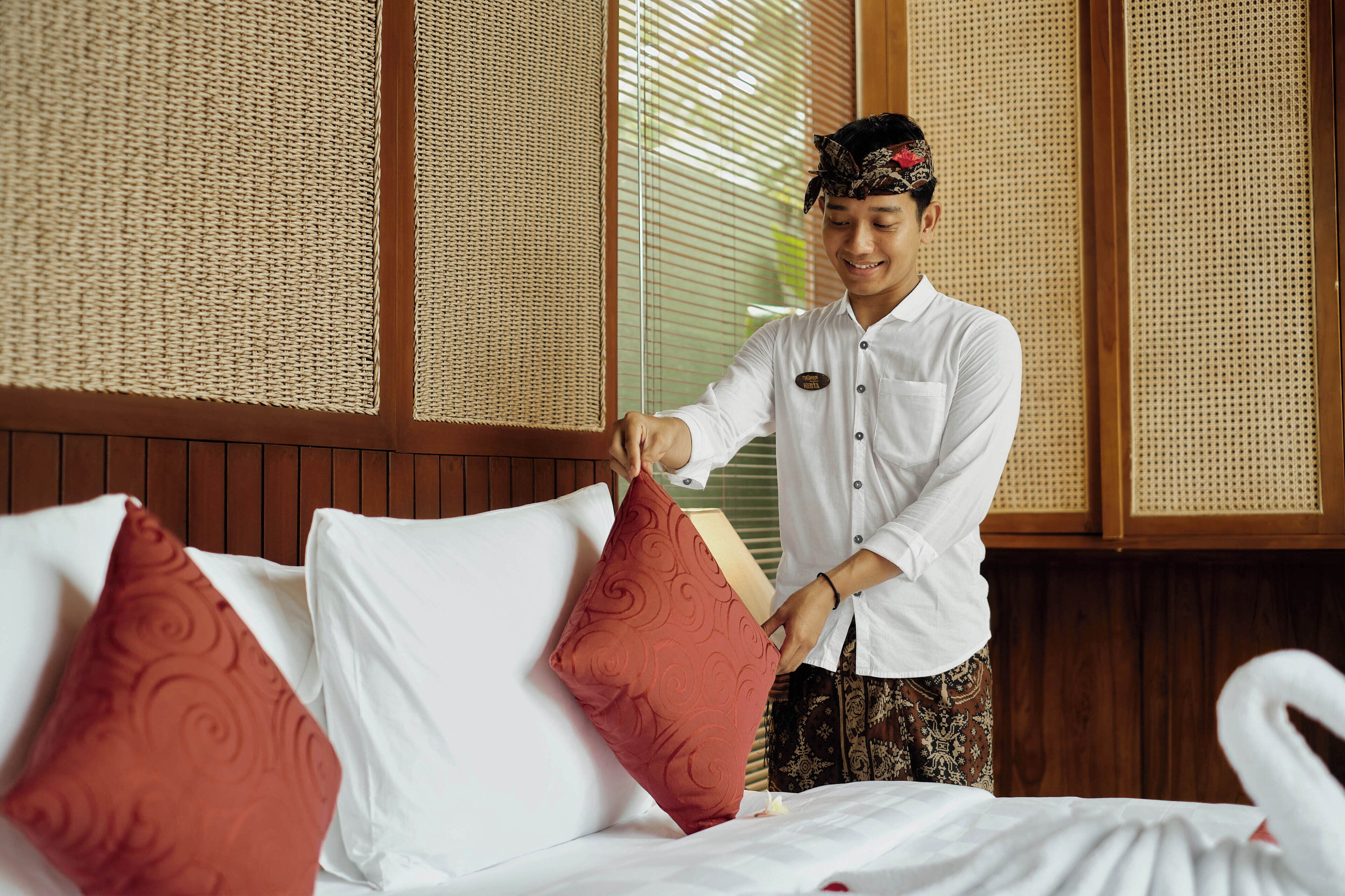 A hotel room with a bed, pillows, and a person adjusting a pillow.