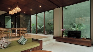 A modern living room with a wooden ceiling, large windows, a sofa, a TV, and a dining area. - Nauma Ubud Villa (Ubud)