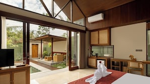 A modern hotel room with a large bed, a TV, a desk, and a view of the outdoor garden. - Nauma Ubud Villa (Ubud)