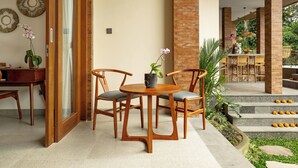 A wooden table with chairs, a potted orchid, and a view of a garden with steps and plants. - Orchid Ubud Cottage (Ubud)