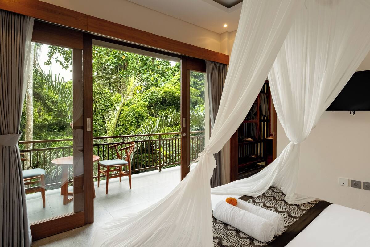 A bedroom with a large sliding glass door leading to a balcony with a view of lush greenery.