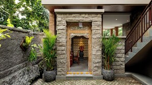 A stone entrance with a wooden door, potted plants, and a staircase leading to an upper level. - Orchid Ubud Cottage (Ubud)