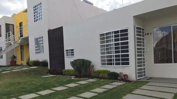 A modern two-story house with a white exterior, a yellow door, and a staircase leading to the upper floor.