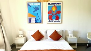 Una camera d'albergo con un letto, due comodini, una lampada, una sedia e due poster incorniciati appesi al muro.