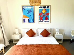 A hotel room with a bed, two nightstands, a lamp, a chair, and two framed posters on the wall. - NEW! Modern and spacious 2-bedroom by the marina in Porto Cupecoy (Sint Maarten)