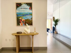 A hallway with a wooden console table displaying a framed picture, a white swan sculpture, and a small vase with reed sticks. - NEW! Modern and spacious 2-bedroom by the marina in Porto Cupecoy (Sint Maarten)