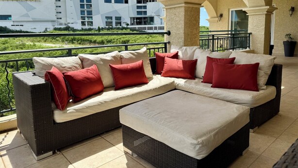 Un'area relax esterna moderna con divano e poggiapiedi, ringhiera di balcone e vista su un edificio sullo sfondo.