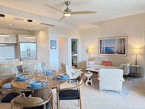 A modern living room with a dining area, a sofa, a coffee table, and a ceiling fan. - NEW ! Elegant and modern 2-Bedroom, with marina and garden view in Porto Cupecoy (Sint Maarten)