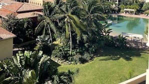 A resort with a pool, palm trees, and buildings with red-tiled roofs. - NEW ! Elegant and modern 2-Bedroom, with marina and garden view in Porto Cupecoy (Sint Maarten)