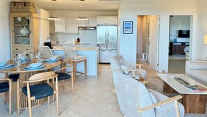 A modern kitchen with white cabinets, a central island, and a dining area with wooden chairs and blue tableware. - NEW ! Elegant and modern 2-Bedroom, with marina and garden view in Porto Cupecoy (Sint Maarten)