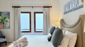 Una camera d'albergo con un letto grande, una testiera e un quadro con dei velieri sulla parete.