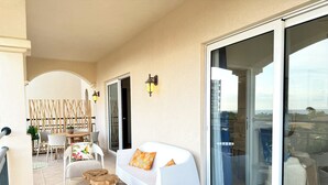 Un balcone con un divano bianco, sgabelli di legno e un'area pranzo con sedie e tavolo.
