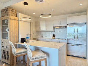 A modern kitchen with a marble countertop, two chairs, a refrigerator, and pendant lighting. - NEW ! Elegant and modern 2-Bedroom, with marina and garden view in Porto Cupecoy (Sint Maarten)