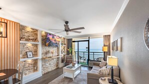 Ein Wohnzimmer mit Steinwand, Deckenventilator, Fernseher und einem Balkon mit Blick.