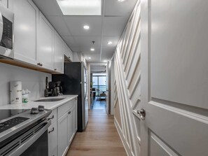 A narrow kitchen with white cabinets, a black countertop, and a stainless steel range hood. - Caravelle 937 (Myrtle Beach)