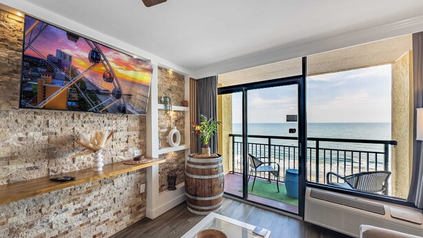 Ein modernes Wohnzimmer mit Stadtbildgemälde, einer Holzkollektion, einem Glastisch und Meerblick durch große Schiebetüren.