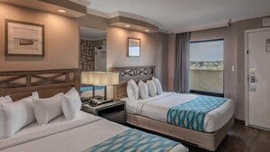 Ein Hotelzimmer mit zwei Betten, einem Schreibtisch, einem Telefon, einer Lampe, einem Spiegel und einem großen Fenster mit Aussicht.
