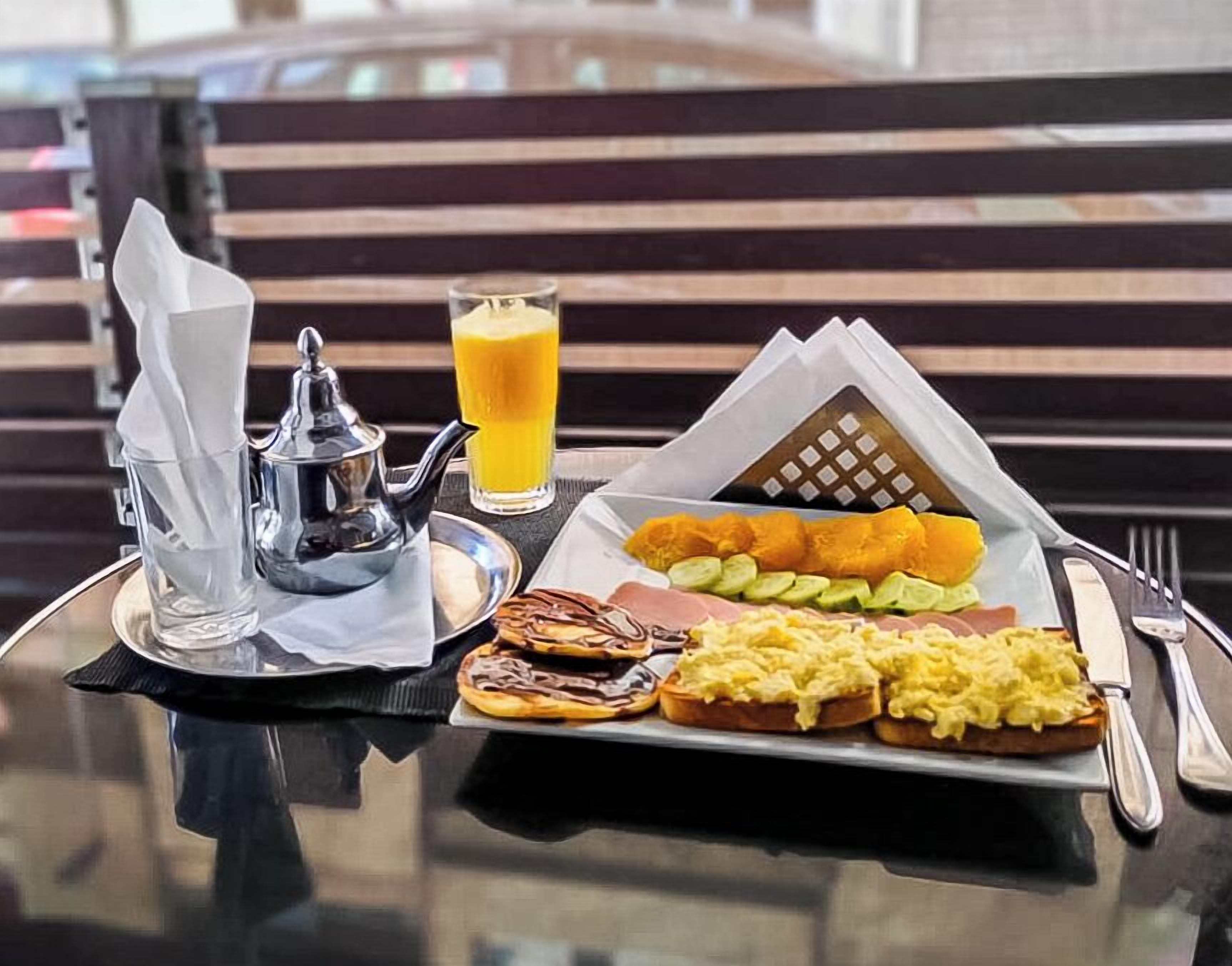 A breakfast tray with scrambled eggs, toast, and orange juice on a table with a napkin and a teapot.