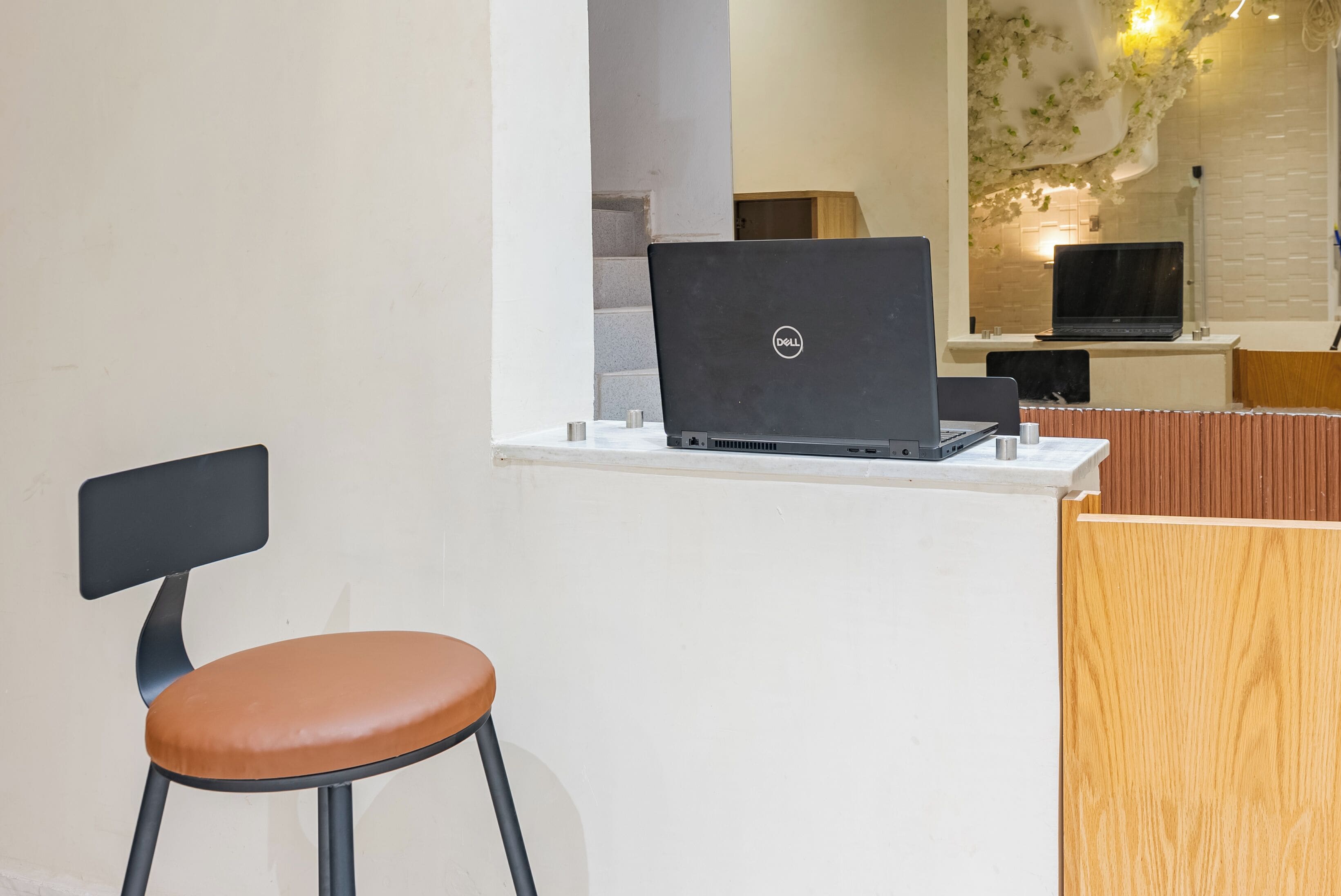 A modern office space with a Dell laptop on a white desk, a brown leather chair, and a wooden reception desk.