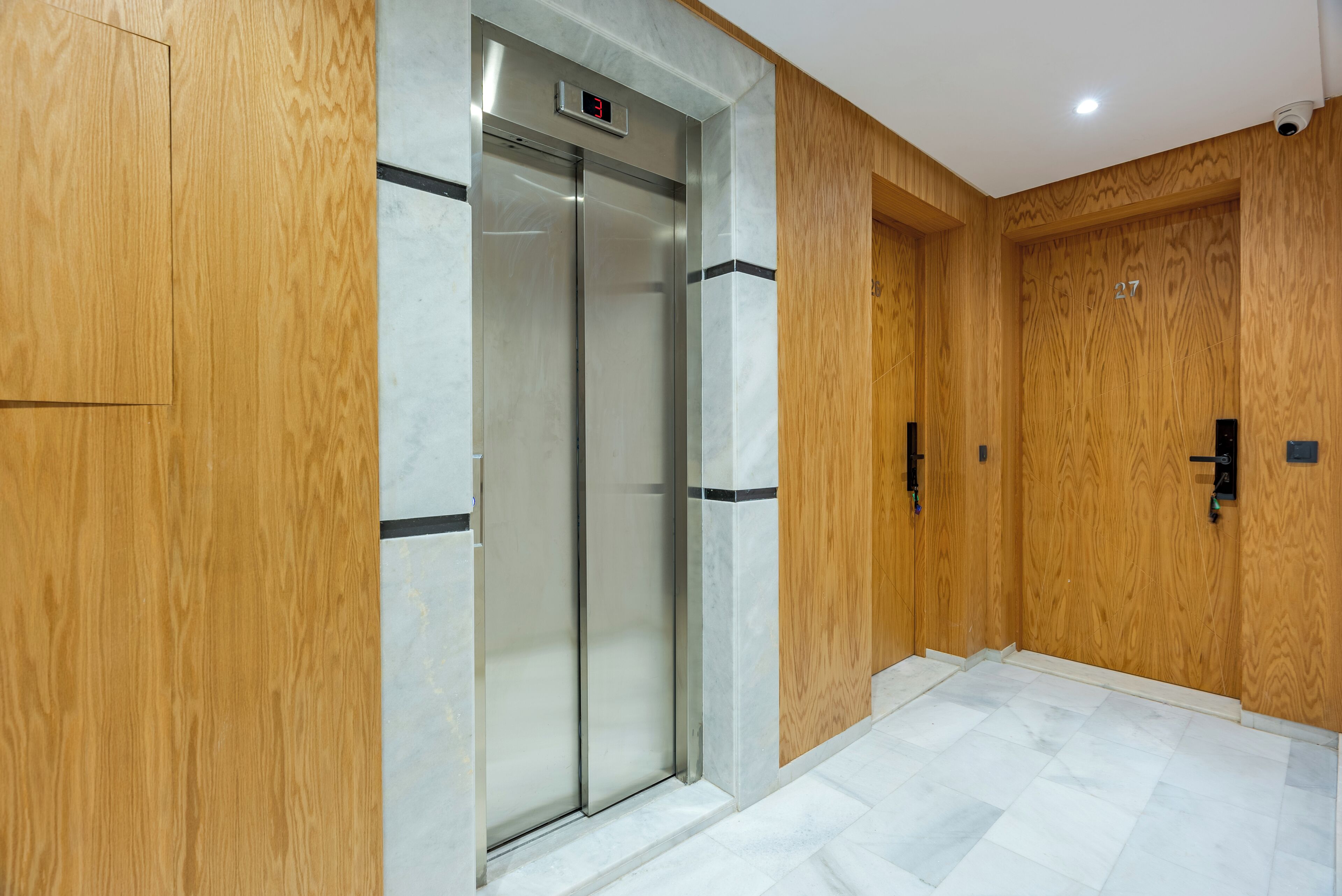 Un ascensor moderno con pantalla digital, paneles de madera y suelo de baldosas.