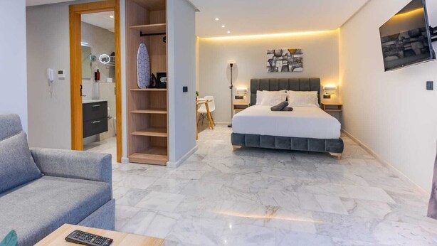 A modern hotel room with a bed, a seating area with a sofa, a walk-in closet, and a bathroom with a mirror and towel rack. - Faya Nova-central stay (Casablanca)