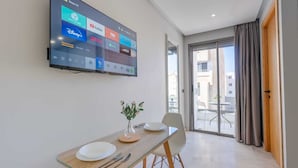 A modern hotel room with a flat-screen TV displaying streaming services, a dining area with a glass table, and a sliding glass door leading to an outdoor balcony. - Faya Nova-central stay (Casablanca)