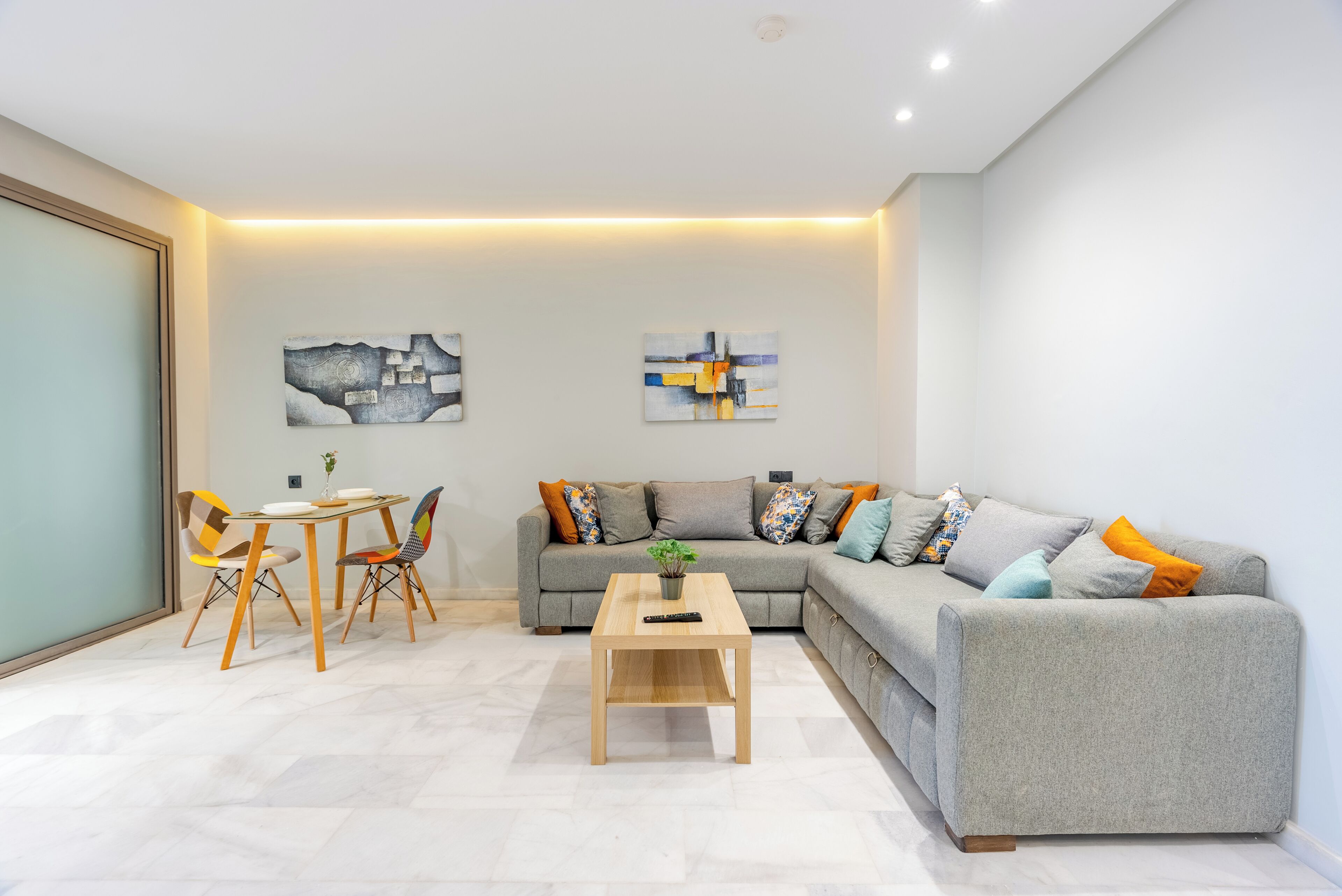 A modern living room with a grey sofa, colorful cushions, a wooden coffee table, and abstract wall art.