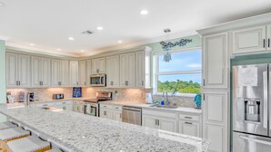 A spacious kitchen with a large island, white cabinetry, stainless steel appliances, and a view of greenery outside. - Oceanfront Rooftop Views w/ 75ft of Dockage (Marathon)