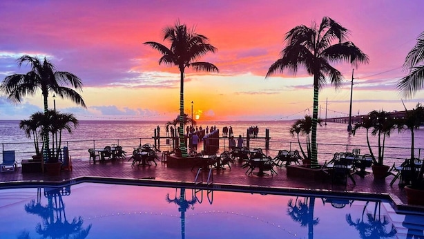 A poolside area with lounge chairs and tables, palm trees, and a sunset view. - Oceanfront Rooftop Views w/ 75ft of Dockage (Marathon)
