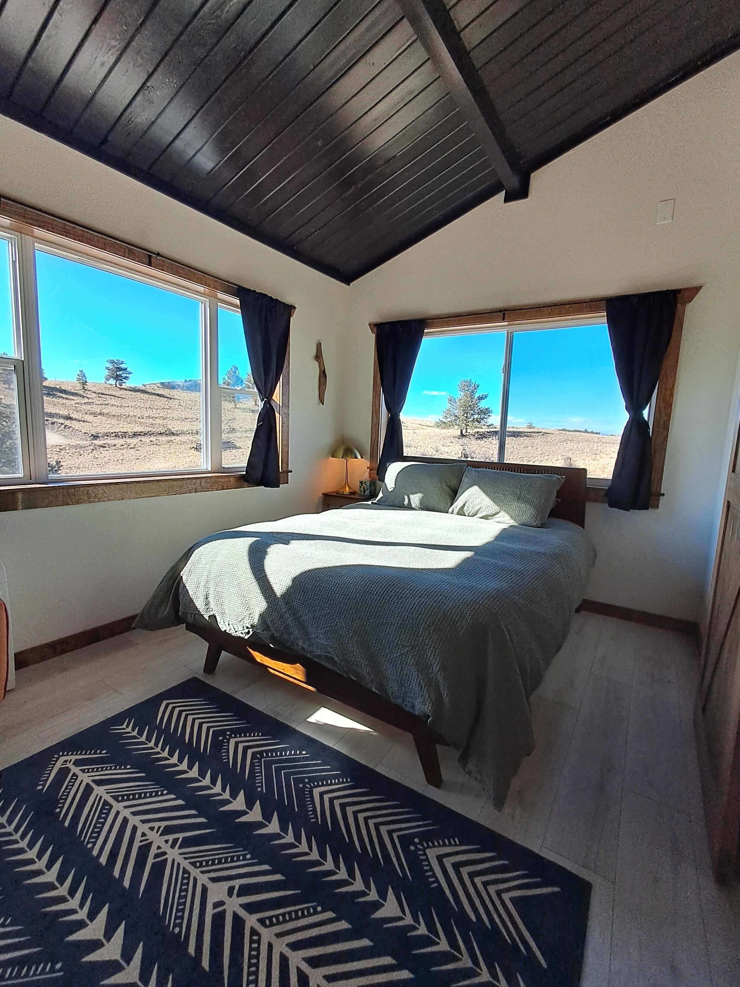 Ein Schlafzimmer mit Bett, großen Fenstern und Blick auf eine Landschaft.