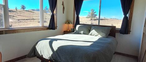 Ein Schlafzimmer mit Bett, großen Fenstern und Blick auf eine Landschaft.