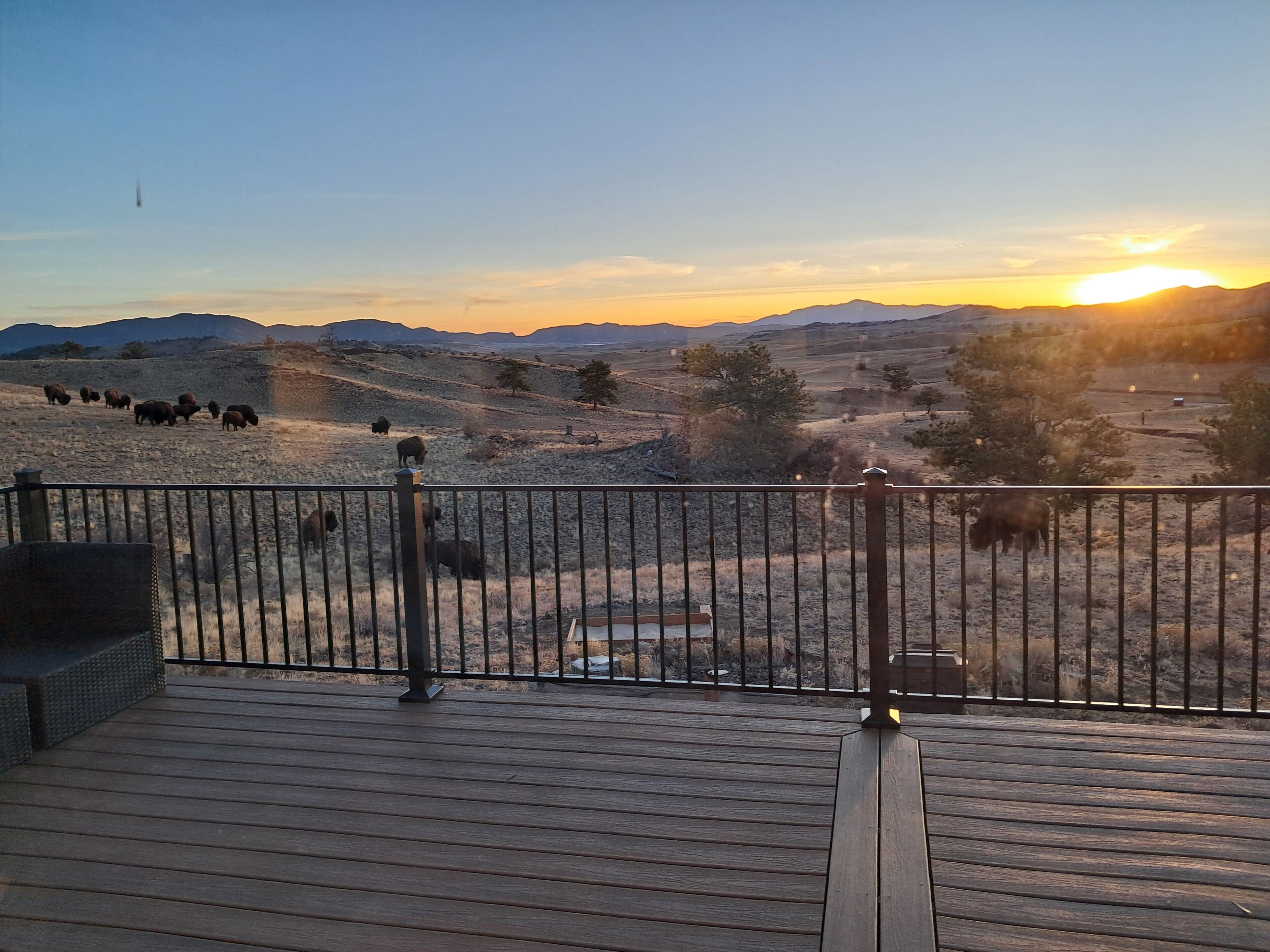 A wooden deck with a metal railing overlooking a dry landscape with scattered trees and hills.