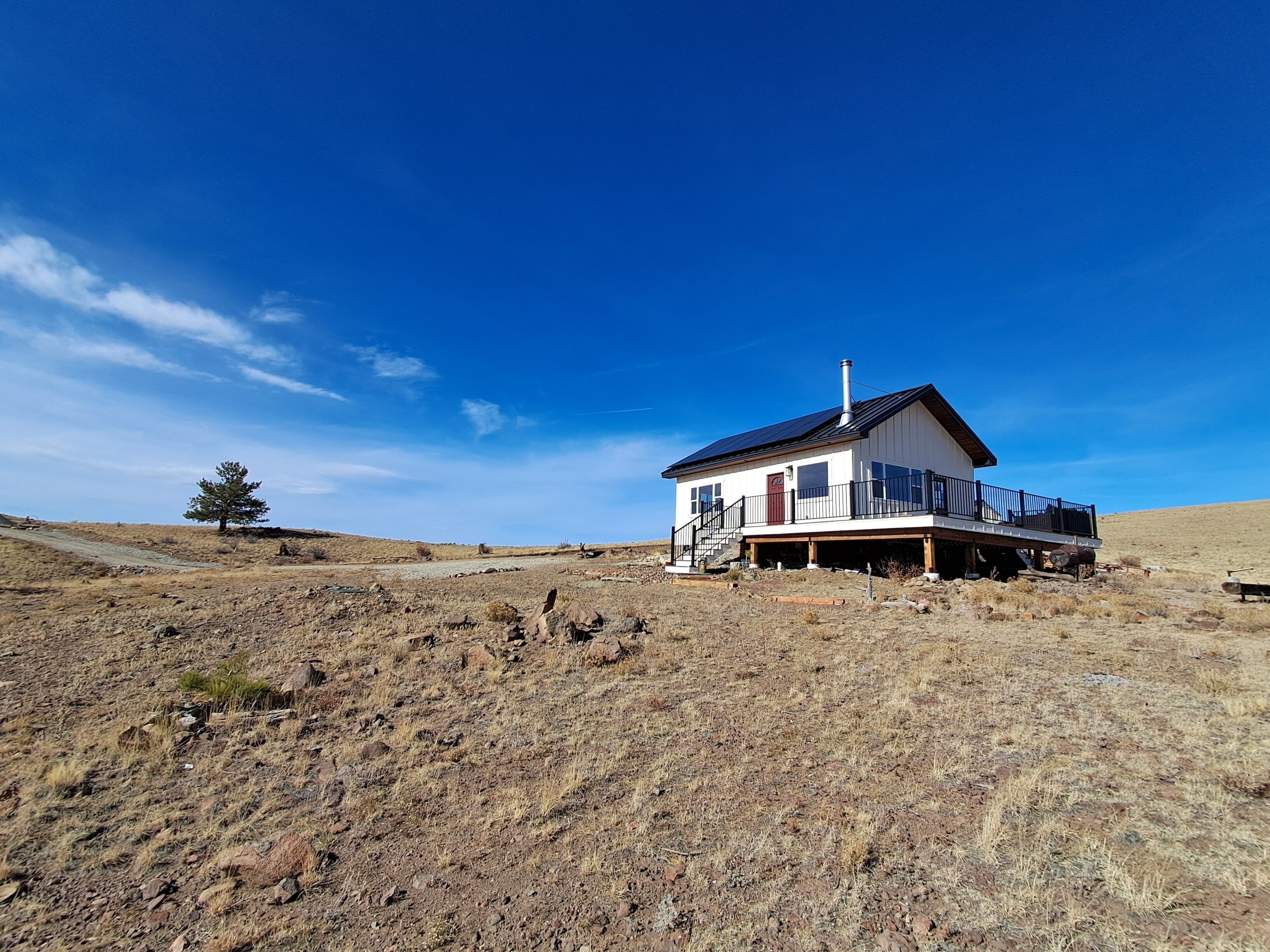 A single-story house with a balcony, situated on a dry, rocky hillside under a clear blue sky.