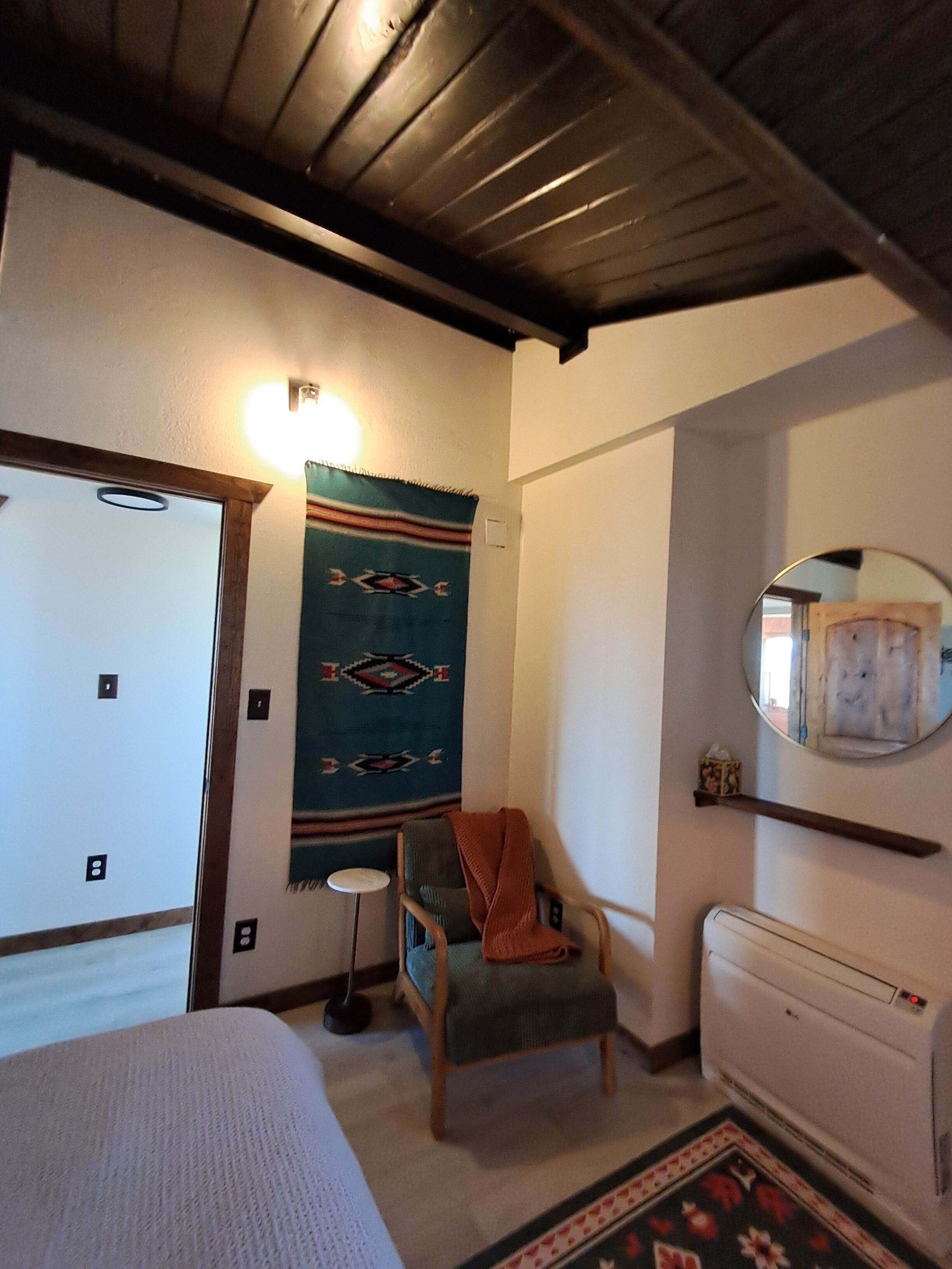 Ein Zimmer mit einem Bett, einem Sessel, einem Heizkörper, einem wandmontierten Spiegel und einer Wanddekoration.