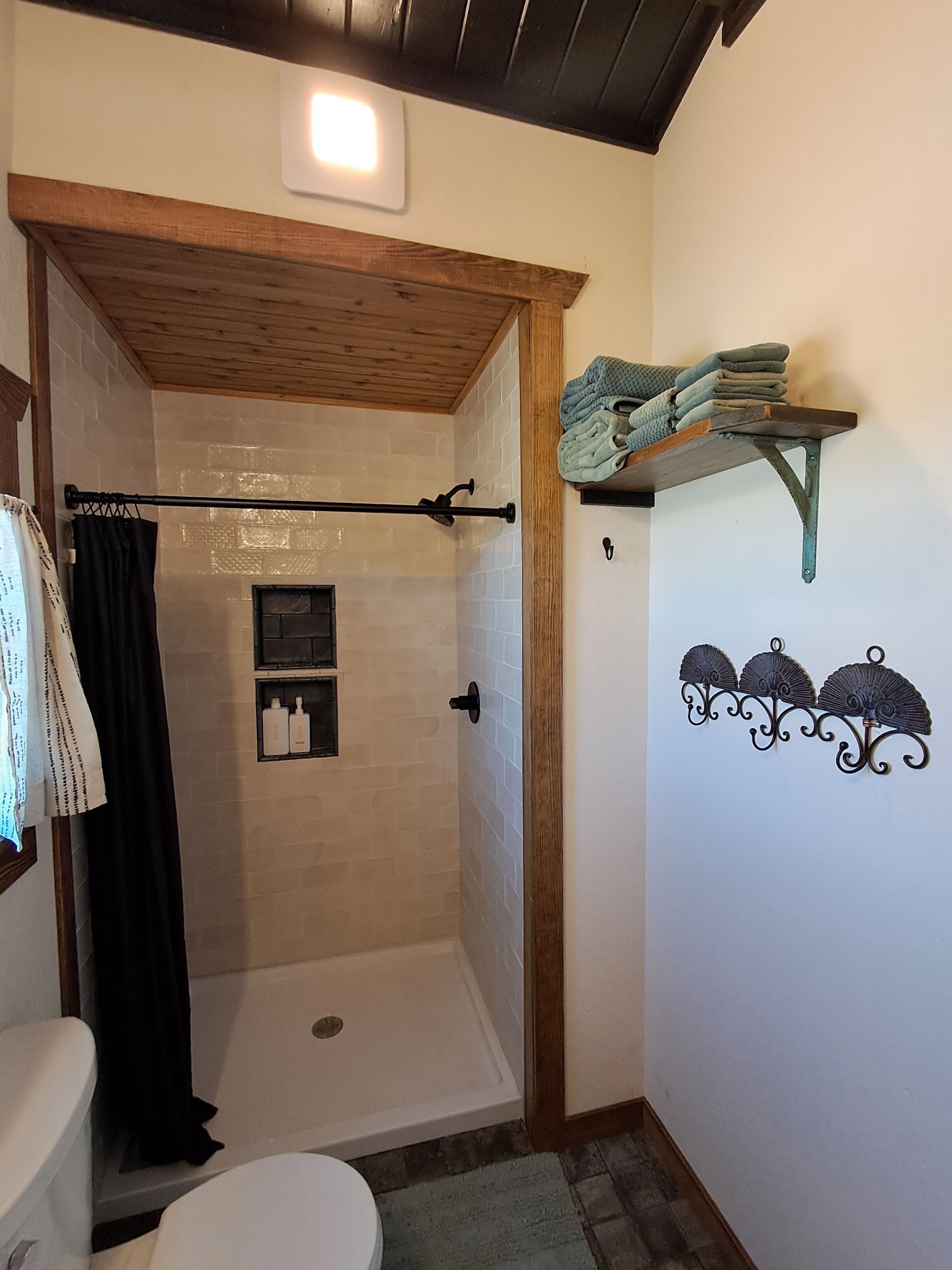 A bathroom with a shower, toilet, and a shelf with folded towels.
