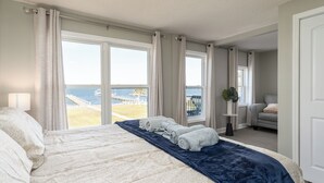 A bedroom with a large bed, a view of the sea, and a balcony. - Soundfront Escape • Private Heated Pool • Dock • Pet Friendly (Emerald Isle)