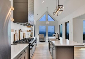 A modern kitchen with a central island, a large window, and a view of the outdoors. - New! Luxe 5BR w/Incredible Views! Hot Tub*Theater (Sevierville)