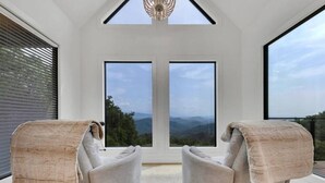 Une pièce avec deux fauteuils placés face à une grande fenêtre donnant sur un paysage montagneux.