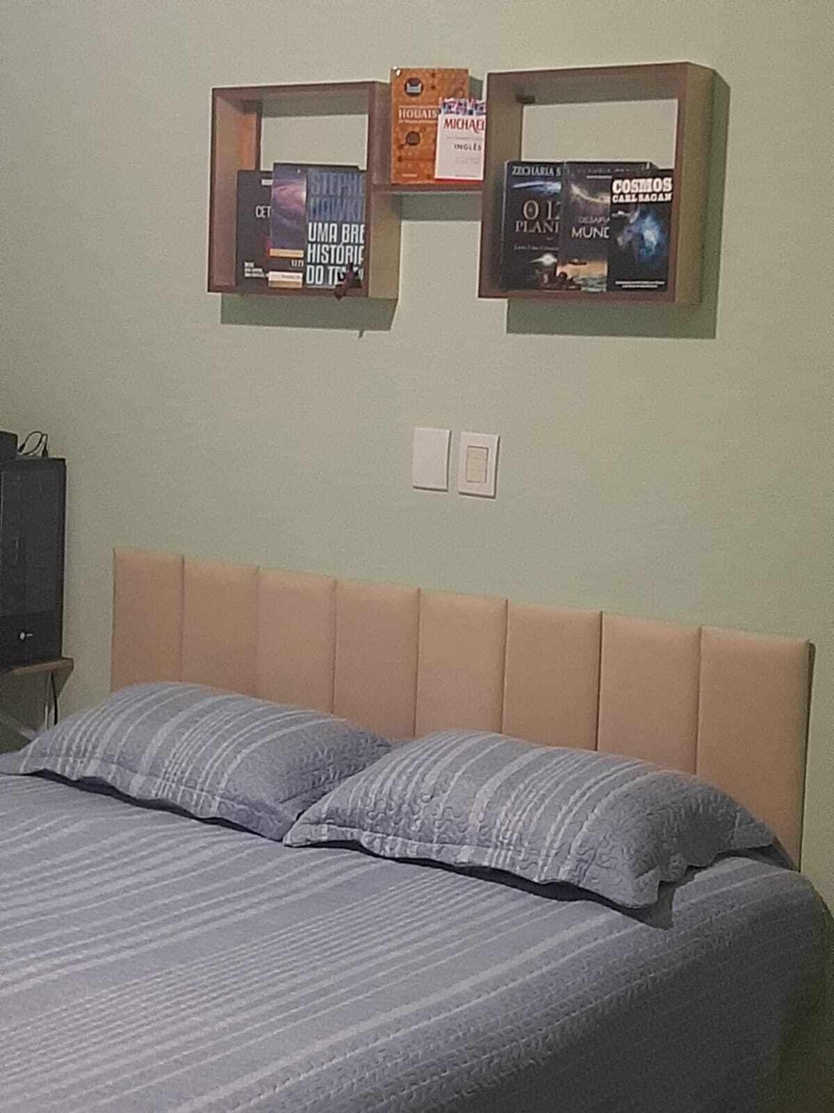 A bedroom with a bed, pillows, a headboard, and two wall-mounted shelves with books.