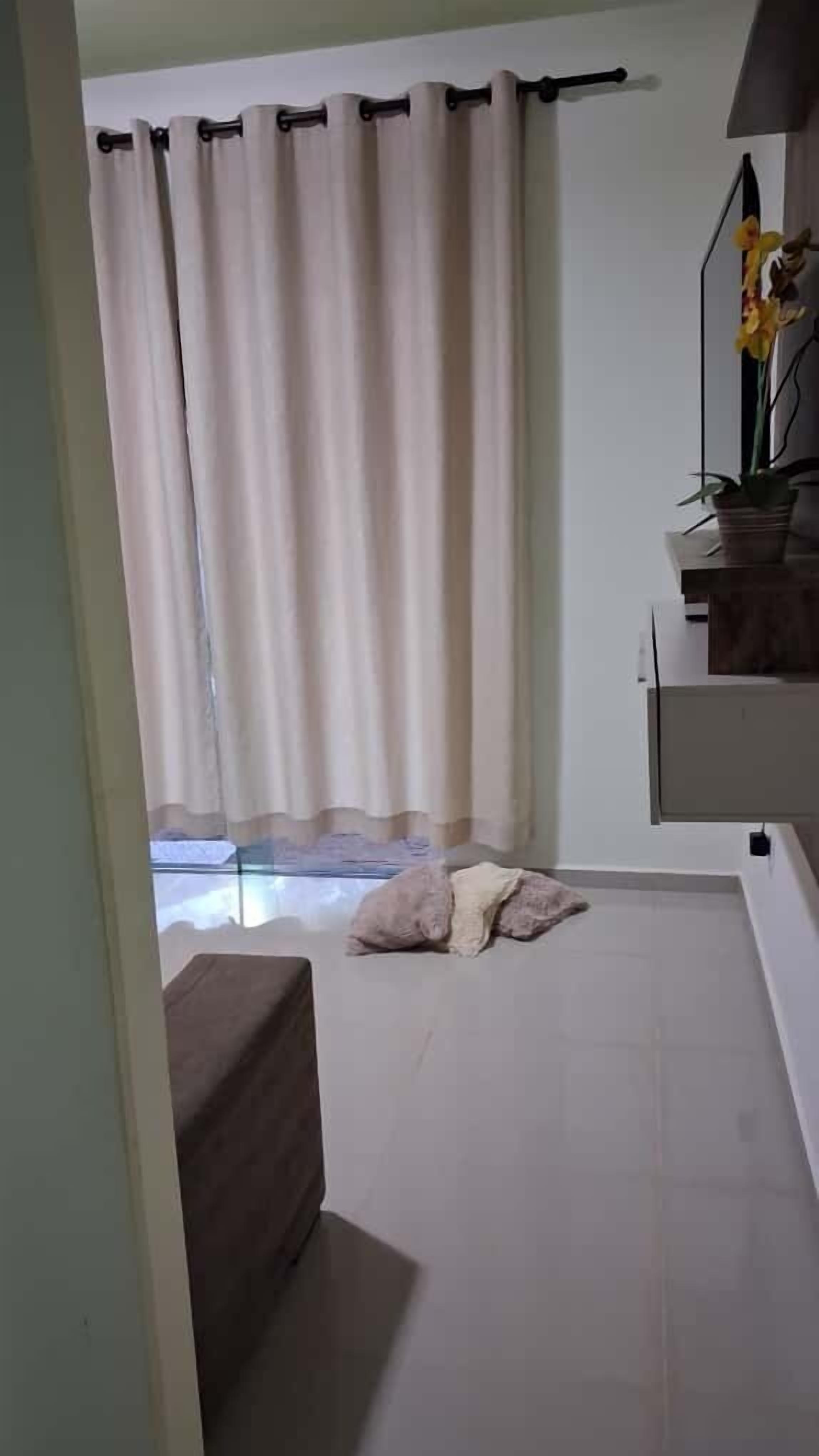 A room with a bed, a small table with a potted plant, and a window with curtains.