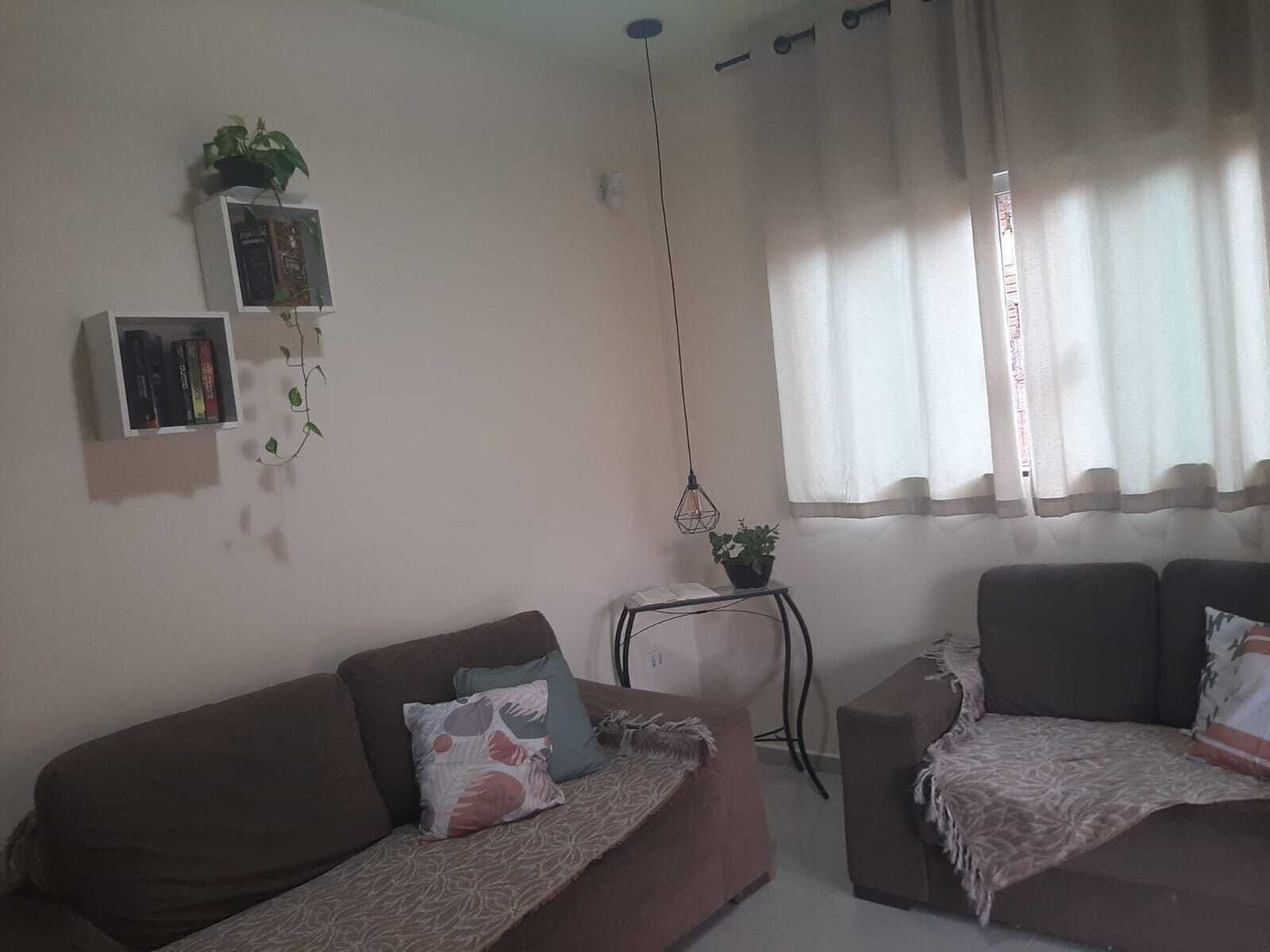 A living room with two sofas, a small side table with a plant, a bookshelf, and a window with curtains.