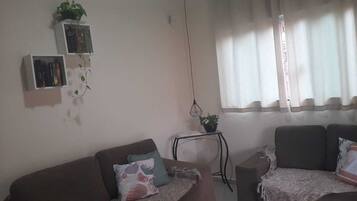 A living room with two sofas, a small side table with a plant, a bookshelf, and a window with curtains.